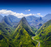 Aerial view of Réunion Island's lush green mountain peaks and river valley under a bright blue sky