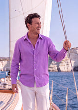 Laos Long Sleeve Linen Shirt in Orchid Belgian linen, front view worn loose over white linen trousers on the deck of a sail yacht.